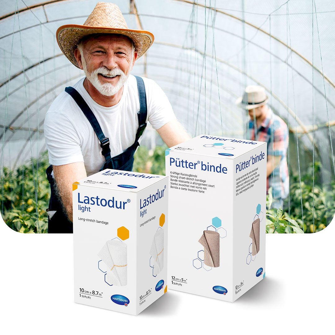 Smiling elderly farmer standing in a greenhouse with HARTMANN compression therapy products (Lastodur light and Pütterbinde) displayed in the foreground.