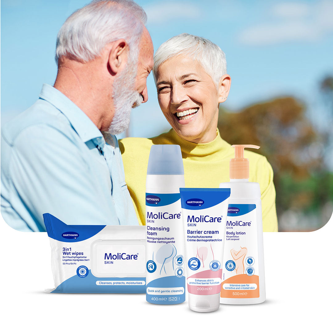 Smiling elderly couple outdoors, with HARTMANN MoliCare Skin Care products (wet wipes, cleansing foam, barrier cream, and body lotion) displayed in the foreground.