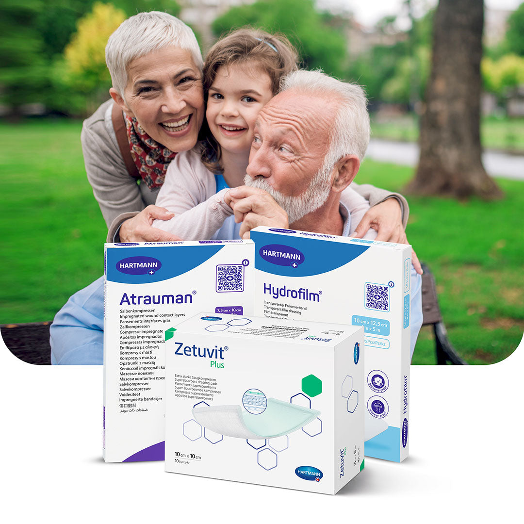 Elderly couple and young girl smiling in a park, with Hartmann wound care products (Atrauman, Hydrofilm, Zetuvit Plus) prominently displayed in the foreground.
