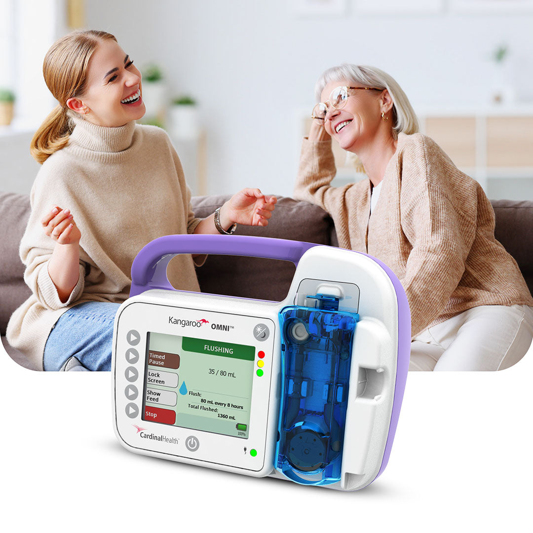 Smiling elderly woman and caregiver enjoying a conversation, with Kangaroo OMNI Enteral Feeding Pump displayed in the foreground, highlighting safe and efficient enteral nutrition delivery.